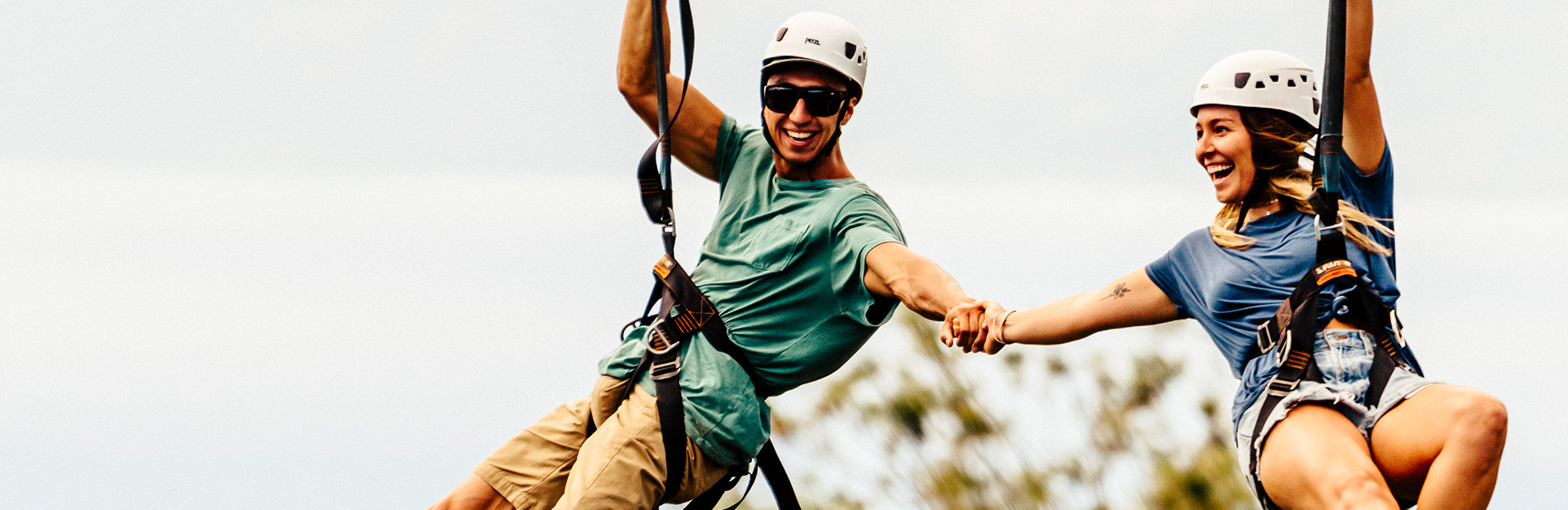 A man and a women holding hands while ziplining side-by-side on Kauai, Hawaii